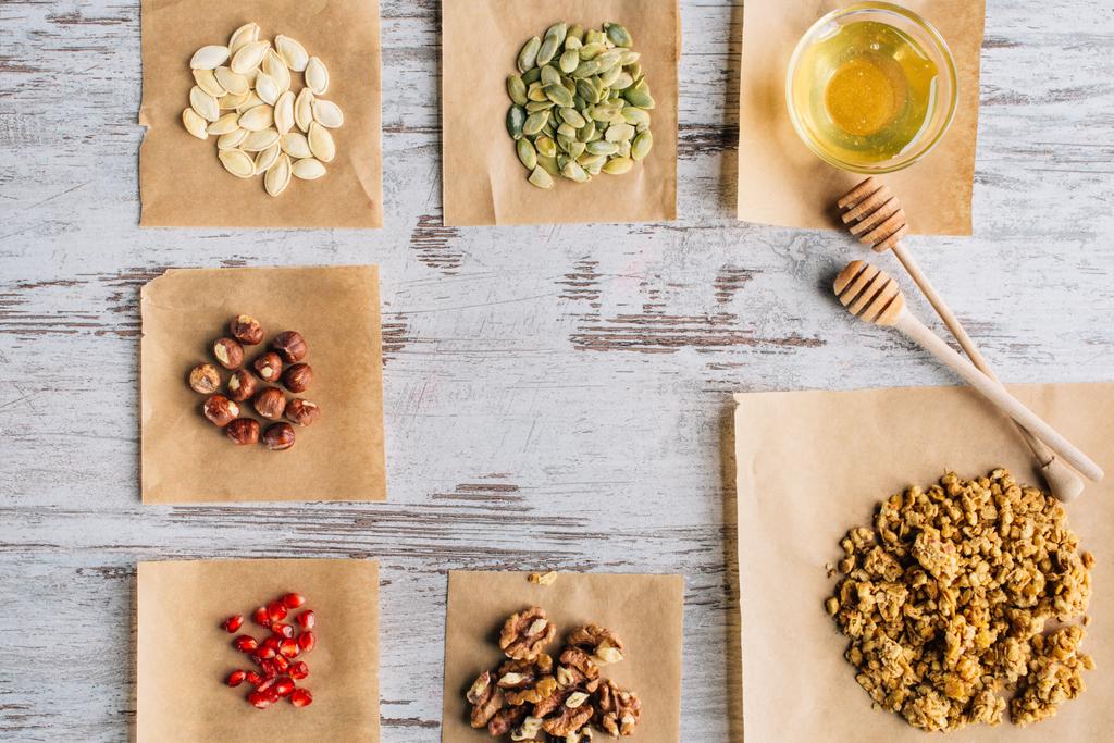 vista dall'alto degli ingredienti della granola sui pezzi di pergamena da forno e sui bastoncini di miele in tavola
 - Foto, immagini