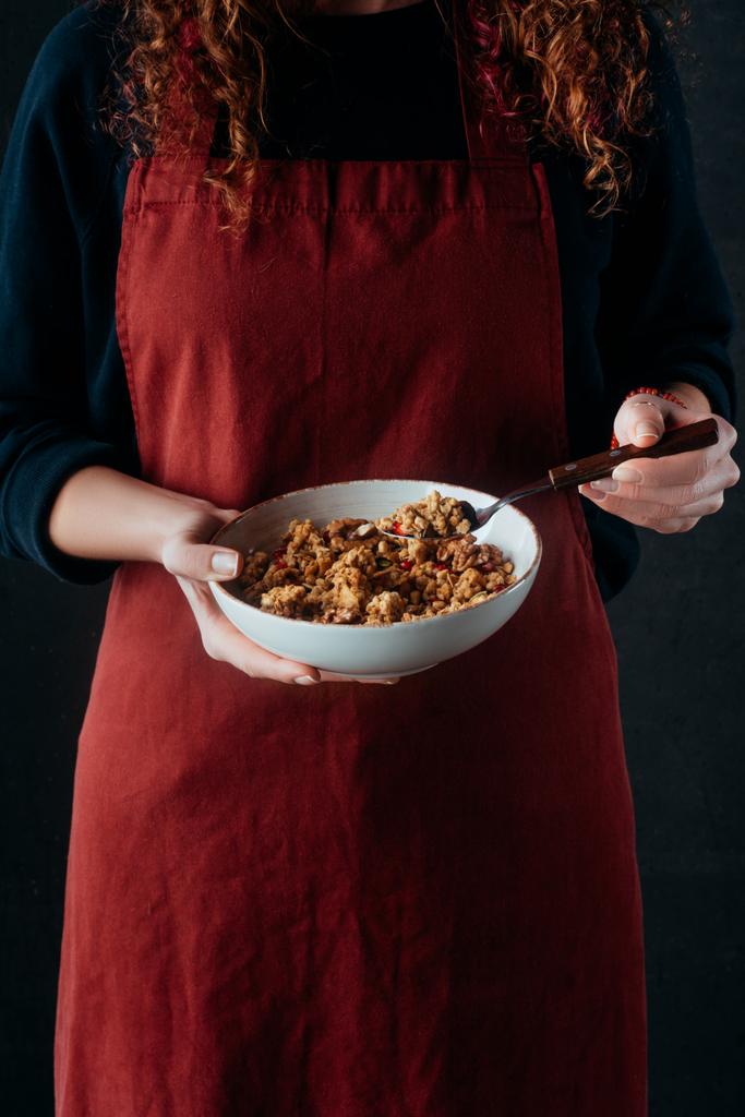 imagem cortada do cozinheiro fêmea segurando tigela com granola e colher
 - Foto, Imagem