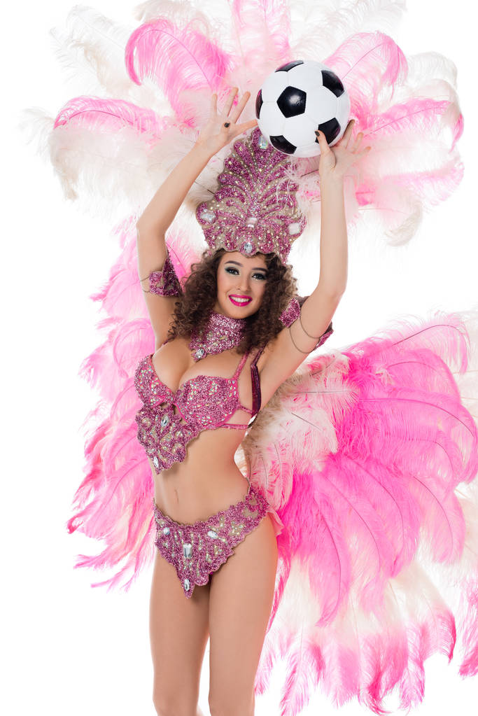 fröhliche Frau im Karnevalskostüm mit rosafarbenen Federn, die einen Fußballball in der Hand hält, isoliert auf weiß - Foto, Bild