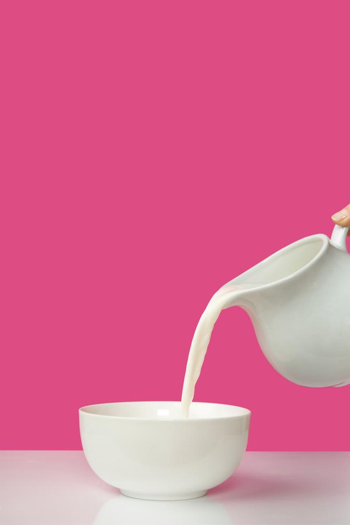 recortado tiro de mano verter leche fresca de jarra a tazón en rosa
       - Foto, imagen