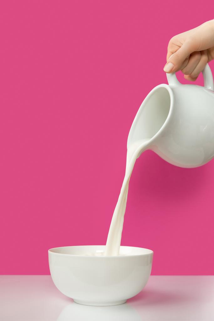 ピンクのボウルに水差しから新鮮な有機牛乳を注ぐ手の部分的なビュー     - 写真・画像