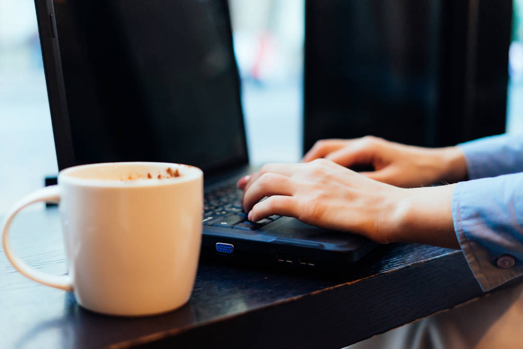 la fille clique sur le clavier dans l'ordinateur portable à côté d'une tasse de café
 - Photo, image
