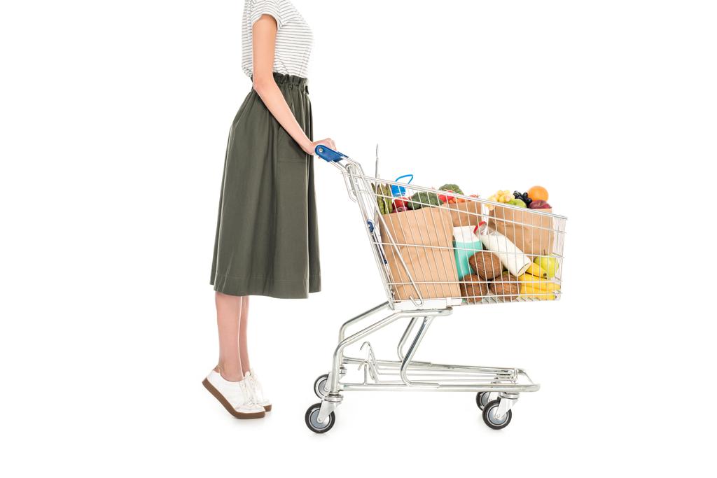 Seitenansicht einer Frau, die mit Einkaufswagen mit Papiertüten und Lebensmittelgeschäft auf weißem Grund steht - Foto, Bild