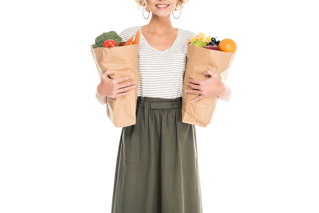 foto recortada de una joven sonriente sosteniendo bolsas de papel con frutas y verduras aisladas en blanco
 - Foto, imagen