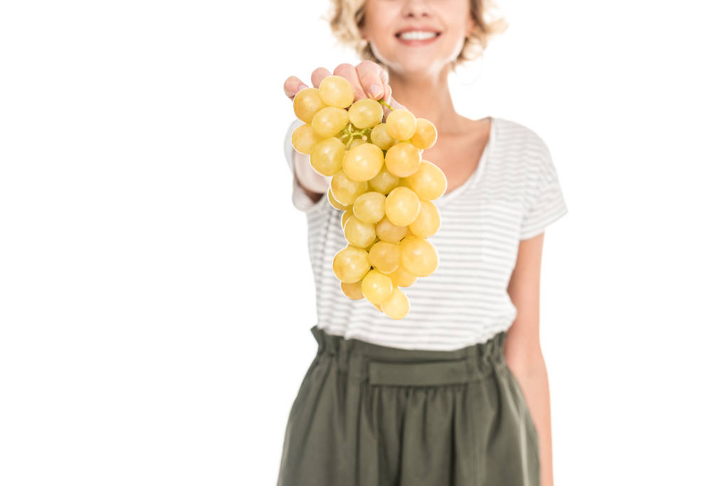 close-up partial view of smiling young woman holding fresh ripe grapes isolated on white - Photo, Image