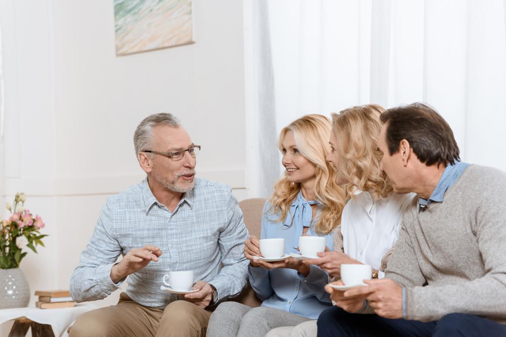 Vanhemmat miehet ja naiset nauttivat aikaa yhdessä juodessaan teetä sohvalla
 - Valokuva, kuva