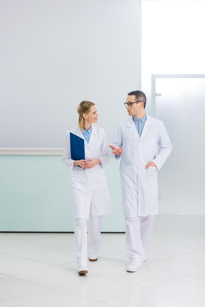 dva doktoři v bílých pláštích s diagnózou mluví v nemocniční chodbě - Fotografie, Obrázek