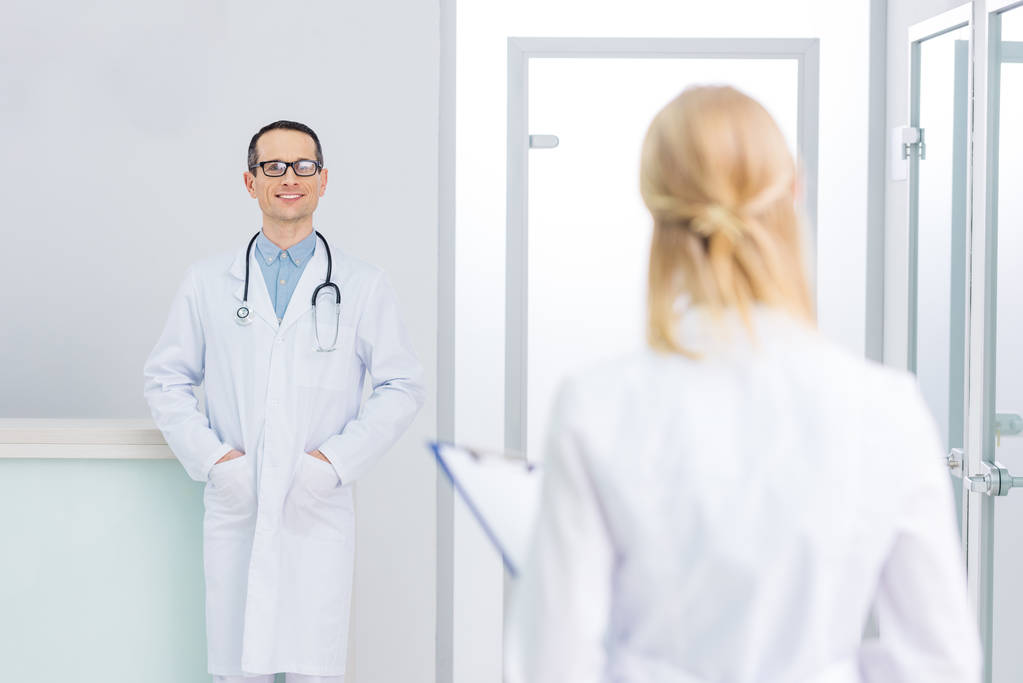чоловічий лікар у білому пальто зі стетоскопом, який дивиться на свого колегу в клініці
 - Фото, зображення