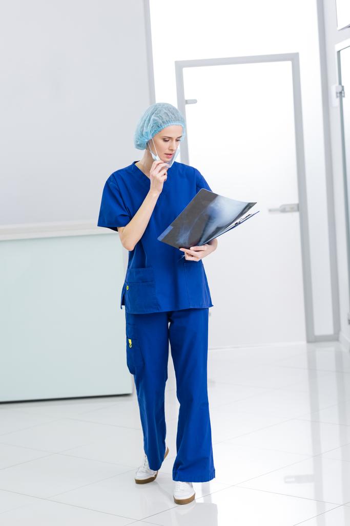 ženské chirurg v lékařské čepici a maska při pohledu na rentgen na klinice - Fotografie, Obrázek