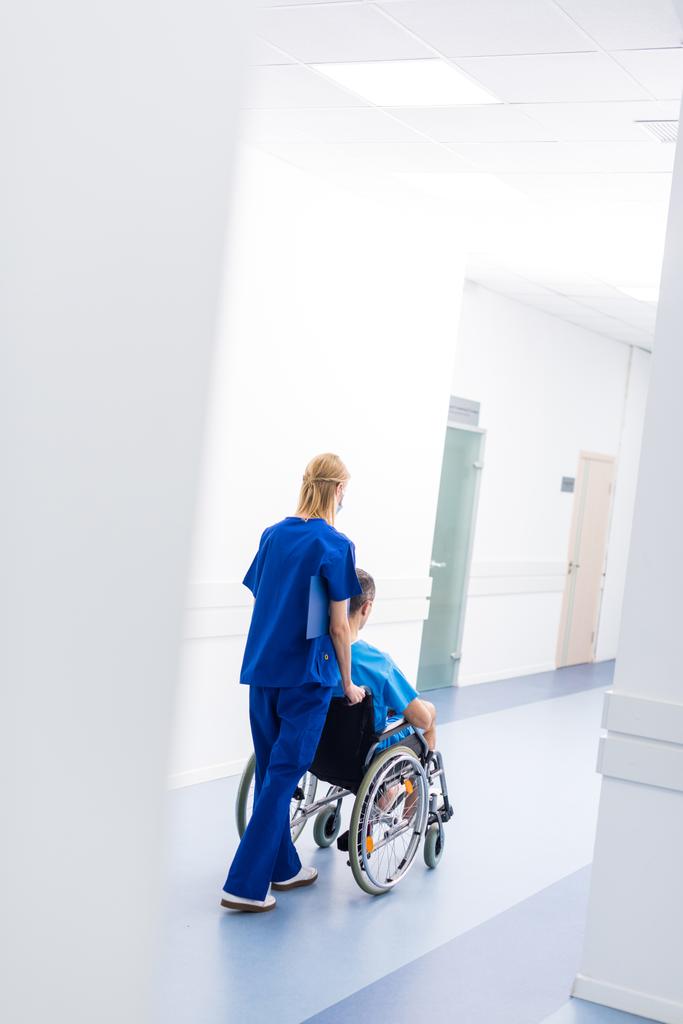 Widok z tyłu pacjenta chirurg i zdenerwowany na wózku inwalidzkim w korytarzu szpitala  - Zdjęcie, obraz