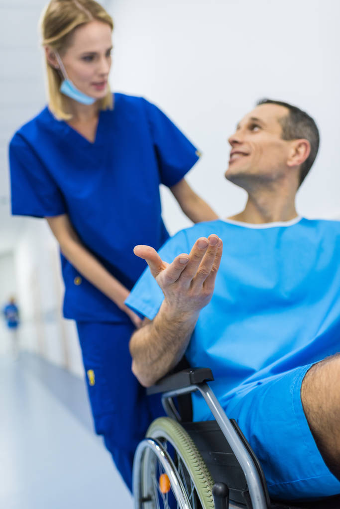 kirurgi puhuu hymyilevän miespotilaan kanssa pyörätuolissa sairaalan käytävällä
  - Valokuva, kuva
