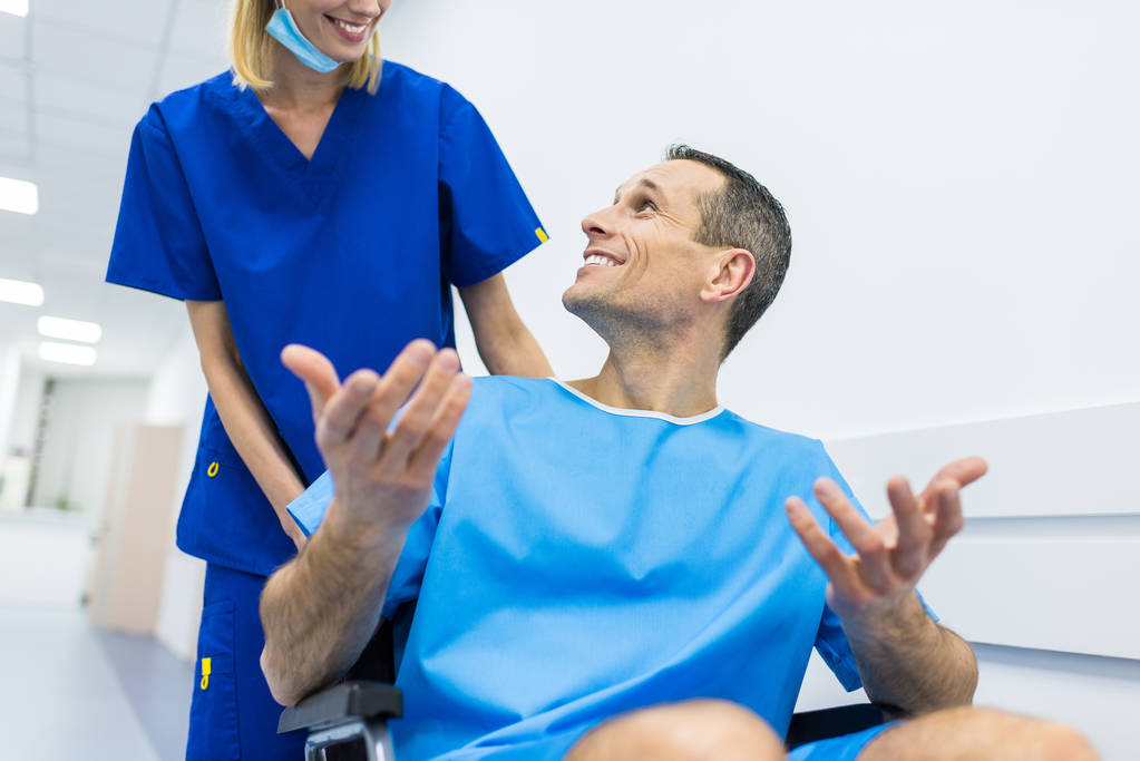 cirujano y paciente masculino sonriente en silla de ruedas en el pasillo del hospital
  - Foto, imagen