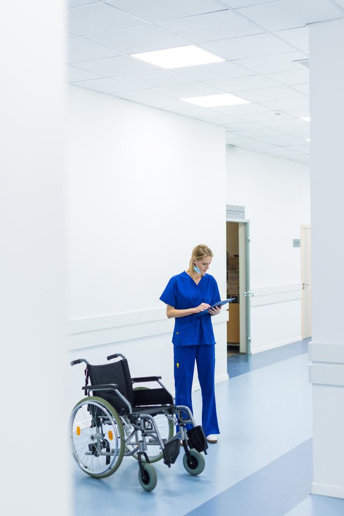 cirujano femenino que lee el diagnóstico y está de pie en silla de ruedas en el pasillo del hospital
 - Foto, imagen