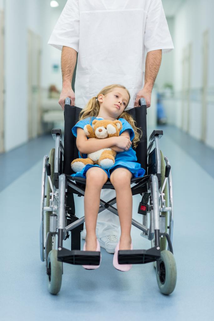 обрезанное изображение доктора, перевозящего ребенка на инвалидной коляске
 - Фото, изображение
