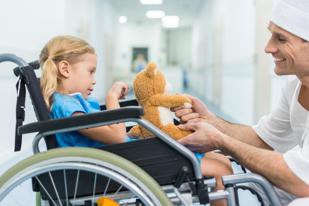 Zijaanzicht van arts en patiënt op rolstoel hand in hand - Foto, afbeelding