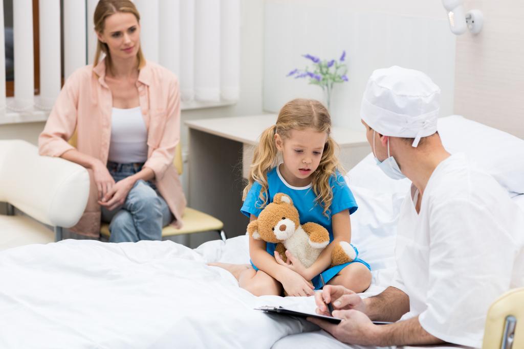 γιατρός, μιλώντας με το παιδί και να κάθεται στο κρεβάτι του νοσοκομείου - Φωτογραφία, εικόνα