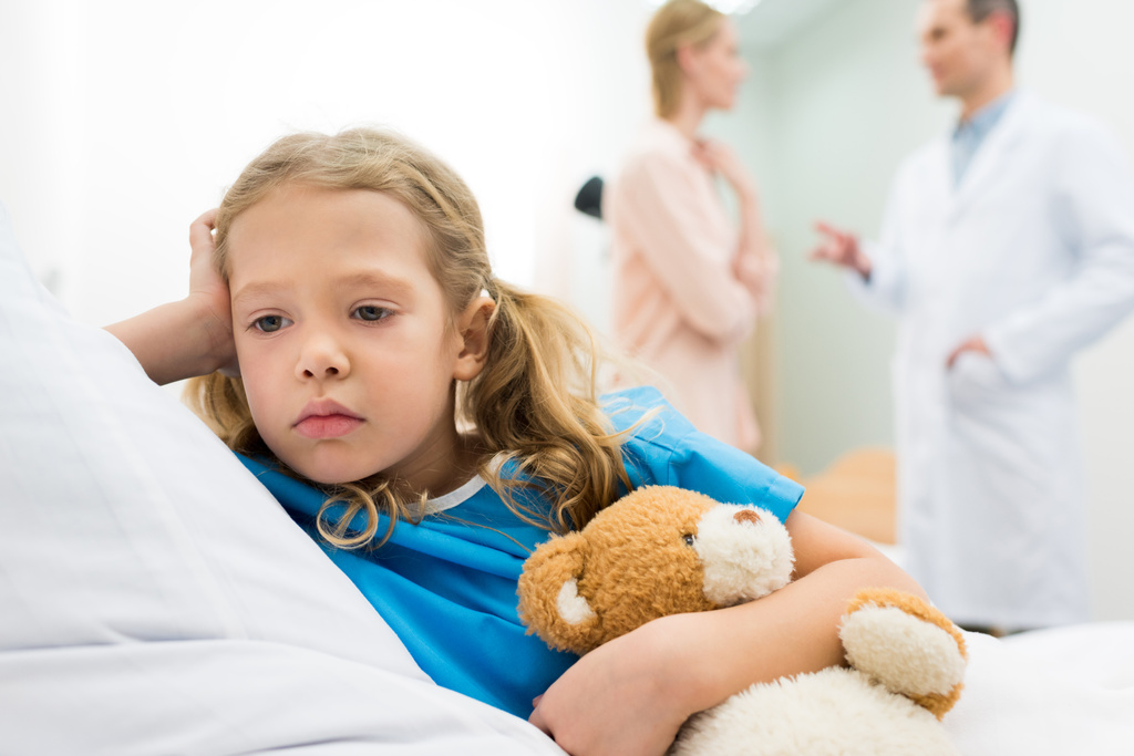 bambino sconvolto sdraiato sul letto d'ospedale mentre la madre parla con il medico
 - Foto, immagini