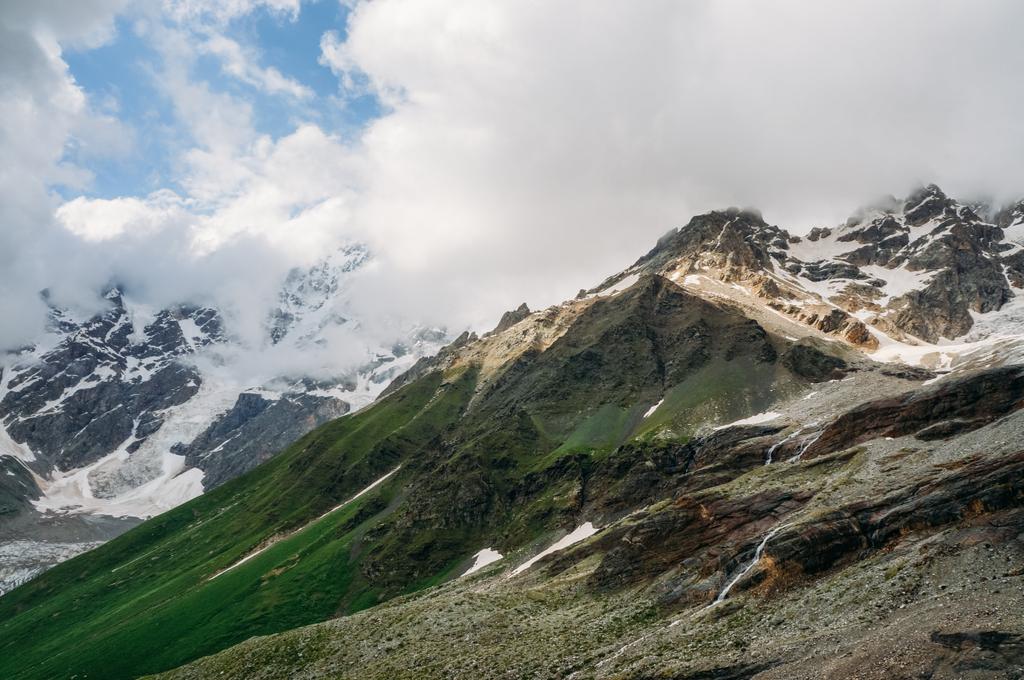 pohled ze zasněžených horských vrcholků s trávou na svazích pod mraky, Ushguli, svaneti, Gruzie  - Fotografie, Obrázek