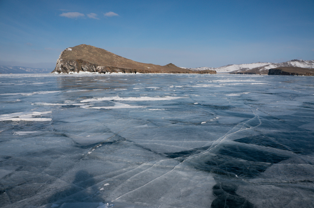 Vista da superfície de água coberta de gelo de formações de lago e rocha no fundo, Rússia, Lago Baikal
 - Foto, Imagem