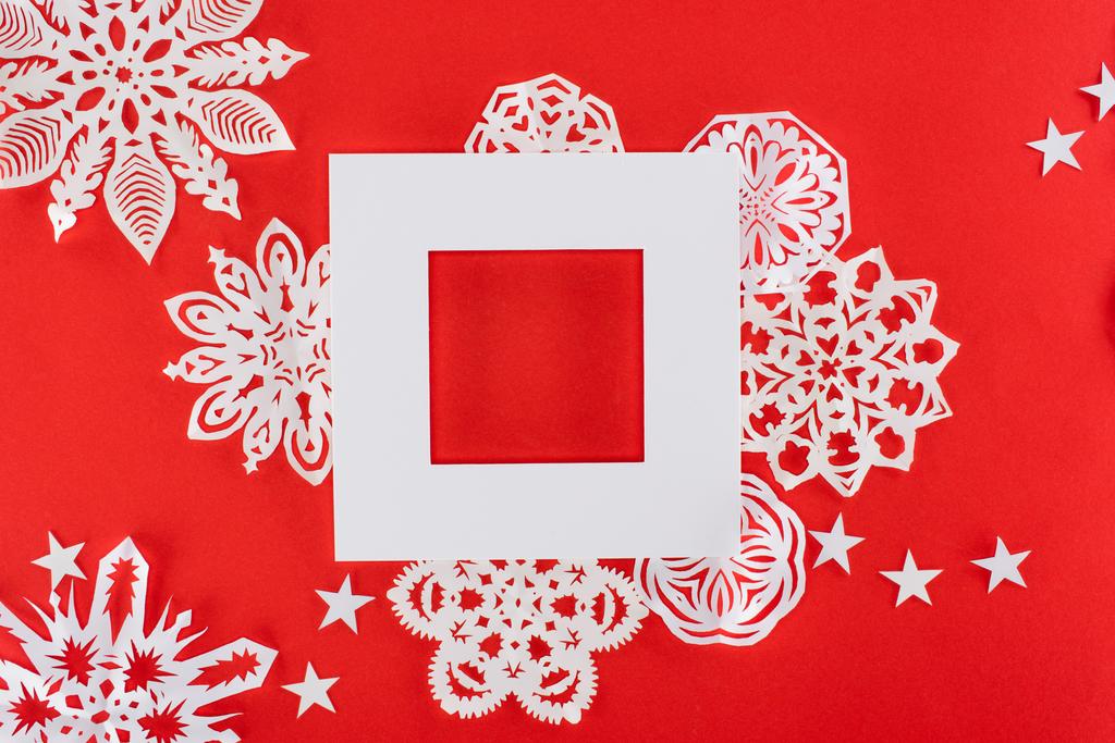 marco de Navidad blanco con estrellas y copos de nieve de papel alrededor, aislado en rojo
   - Foto, Imagen