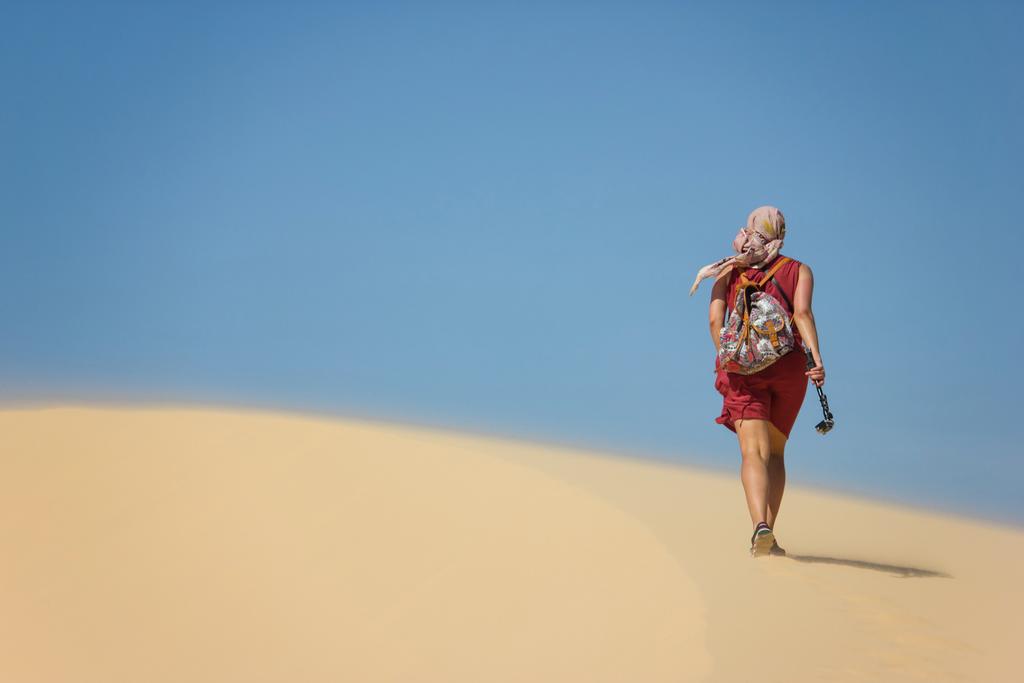 Rückansicht einer einsamen Frau mit Rucksack, die in der Wüste wandert, Vietnam, Phan Thiet - Foto, Bild