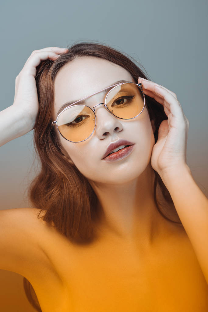 Zmysłowa dziewczyna pozuje w żółte okulary, na szarym tle - Zdjęcie, obraz