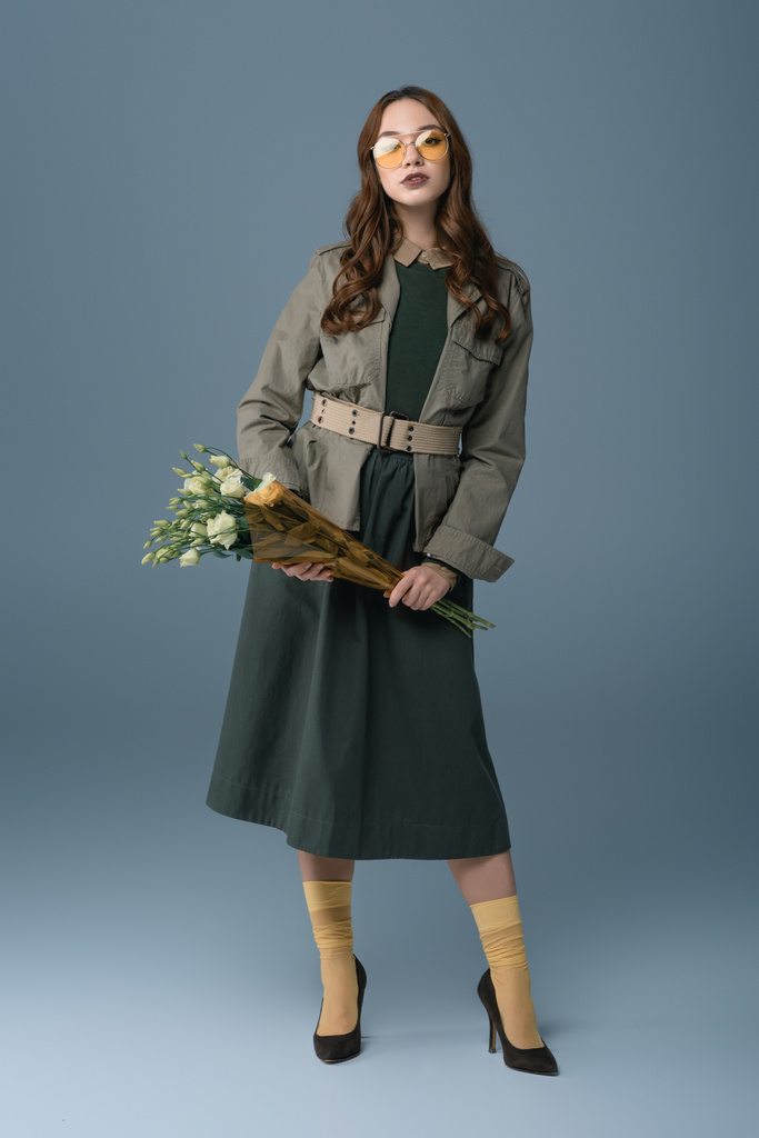 piękna dziewczyna modny pozowanie w jesienny strój z bukietem kwiatów, na szarym tle - Zdjęcie, obraz