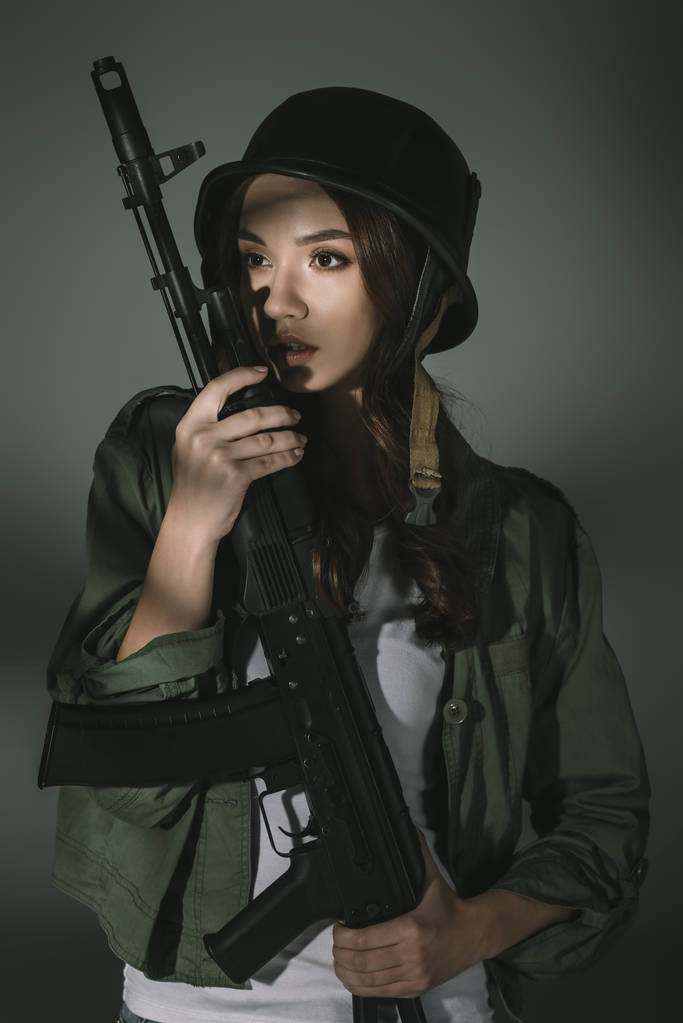 jolie jeune fille en casque militaire avec fusil, sur gris avec des ombres
 - Photo, image