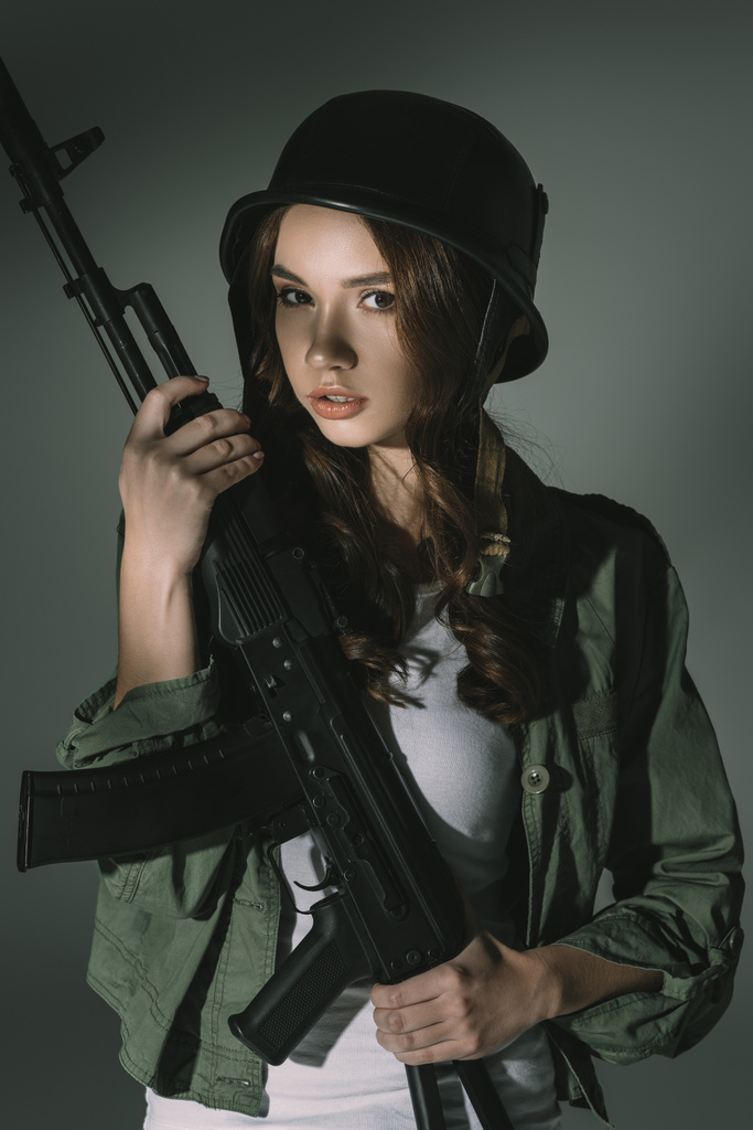 atraktivní mladá dívka v vojenská helma s puškou, Grey se stíny - Fotografie, Obrázek