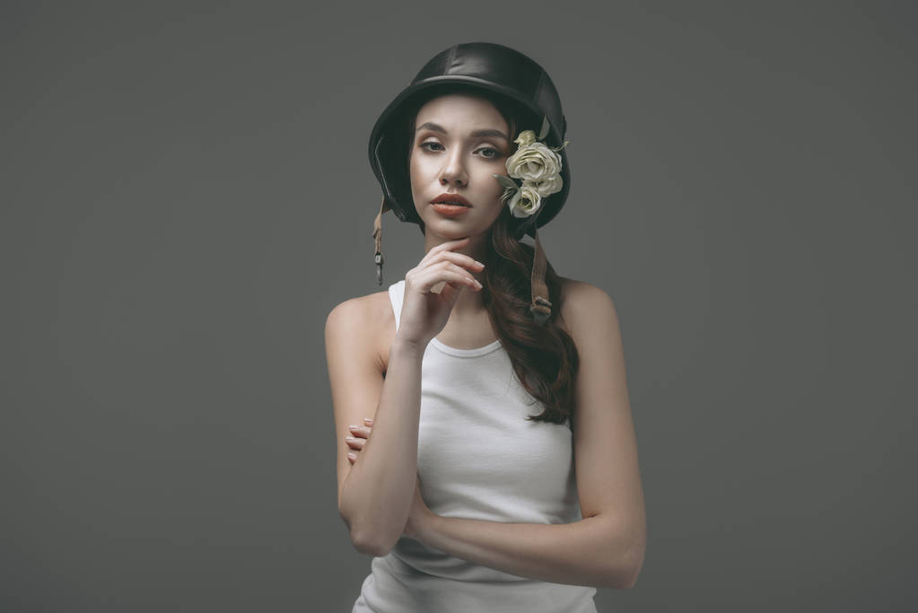 beautiful young girl in military helmet with flowers, isolated on grey - Photo, Image