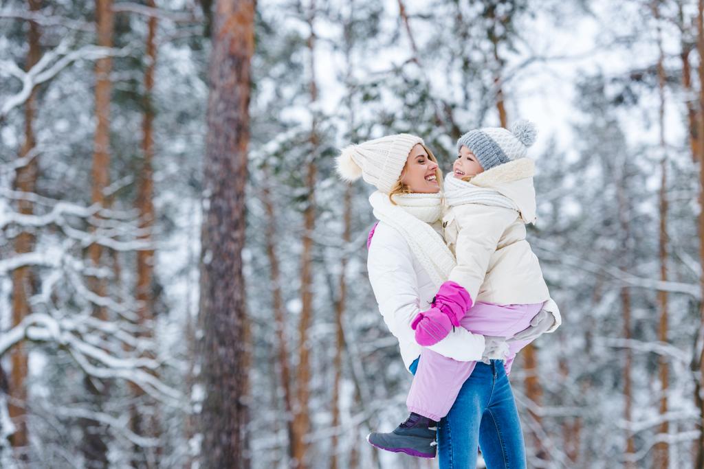 boční pohled matky drží malou dceru v ruce v zimě lese - Fotografie, Obrázek