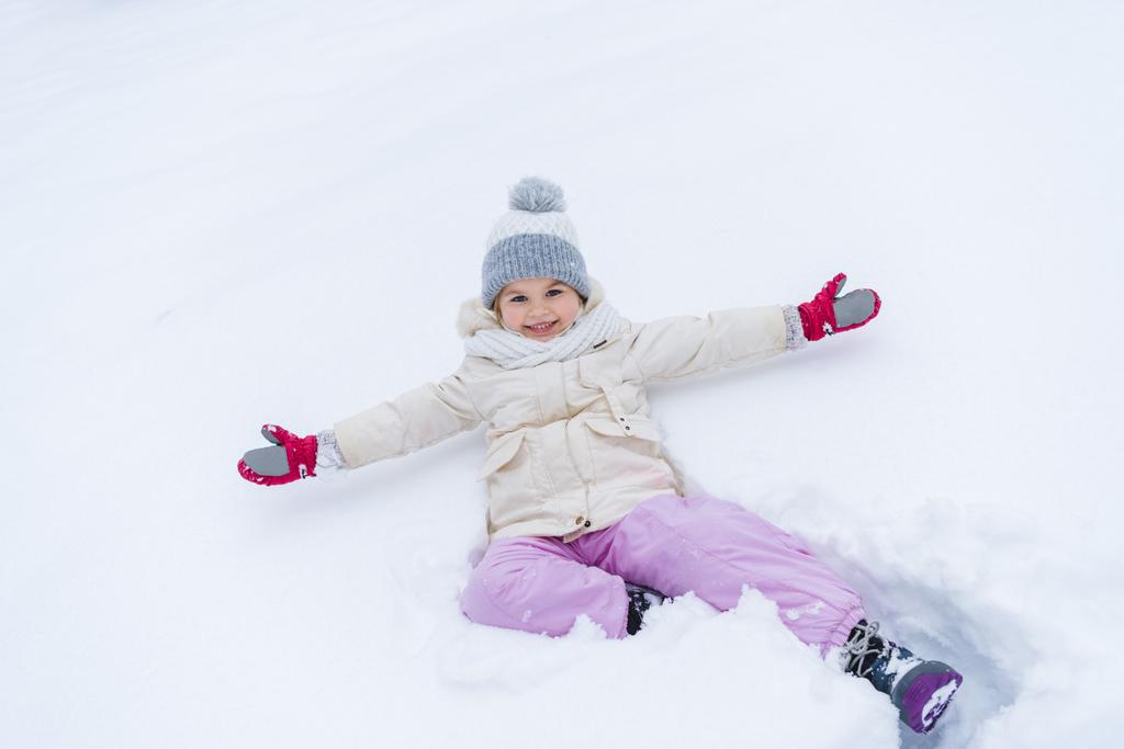 rozkošné malé dítě s otevřenou náručí leží na sněhu a usmívá se na kameru - Fotografie, Obrázek