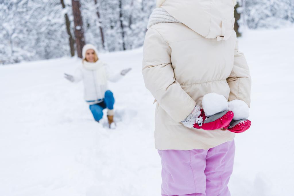 ritagliato colpo di piccola figlia in possesso di palle di neve e felice madre inginocchiato dietro nel parco invernale
 - Foto, immagini