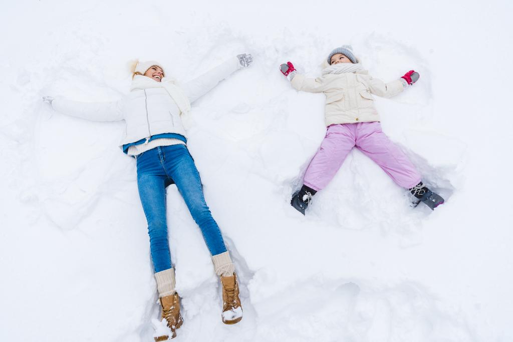 vista ad alto angolo di madre e figlia felice facendo angeli di neve e sorridendo l'un l'altro
 - Foto, immagini