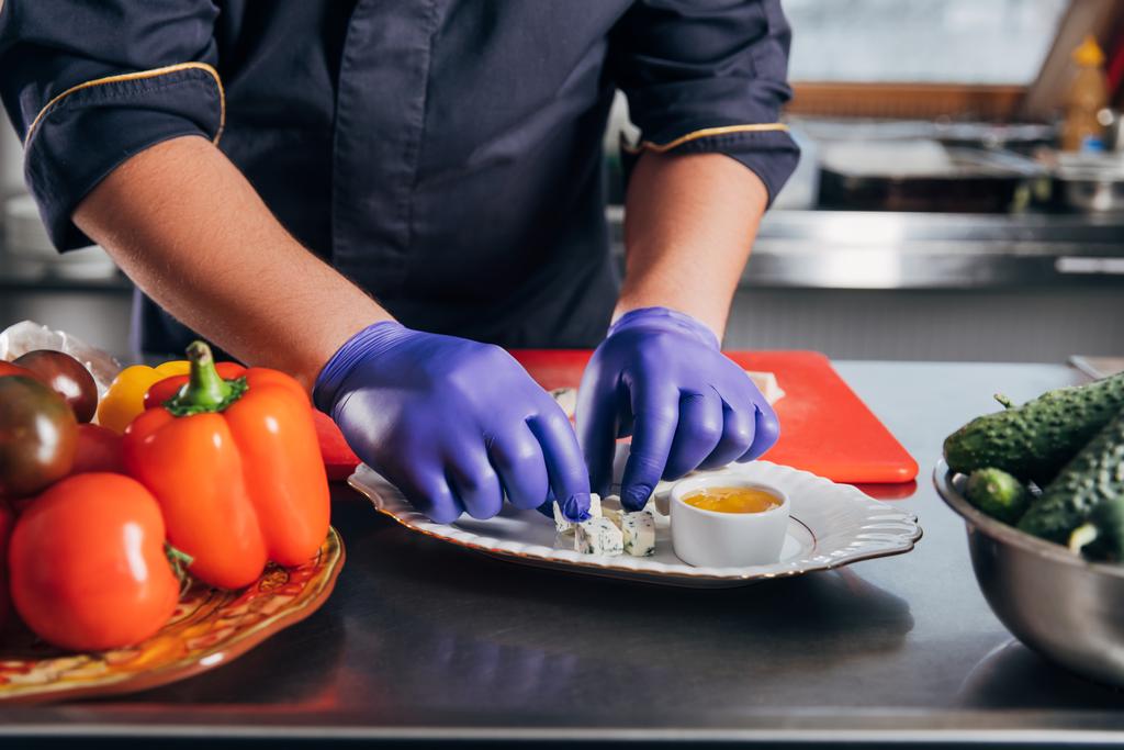 обрезанный снимок шеф-повара, кладущего кусочки сыра на тарелку на кухне
 - Фото, изображение
