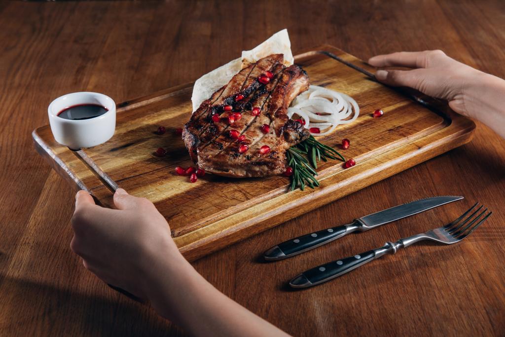 plan recadré d'une femme tenant un steak grillé servi avec de la sauce et des graines de grenade sur une planche en bois
 - Photo, image