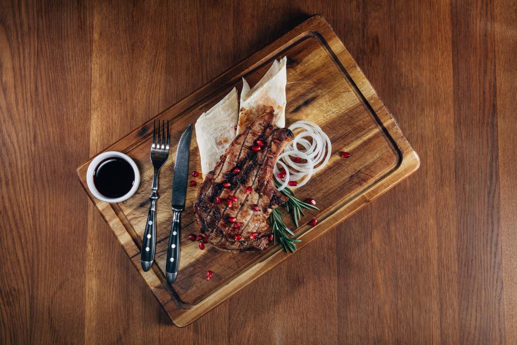 bovenaanzicht van gegrilde steak geserveerd met saus en de granaatappel zaden op houten bord - Foto, afbeelding