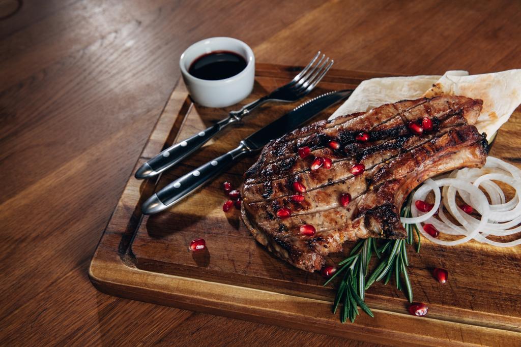 close-up shot of grilled steak served with sauce and pomegranate seeds on wooden board - Photo, Image