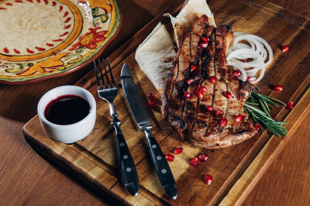 Detailní záběr grilovaný steak podávaný s omáčkou a granátové jablko semena na dřevěné desce - Fotografie, Obrázek
