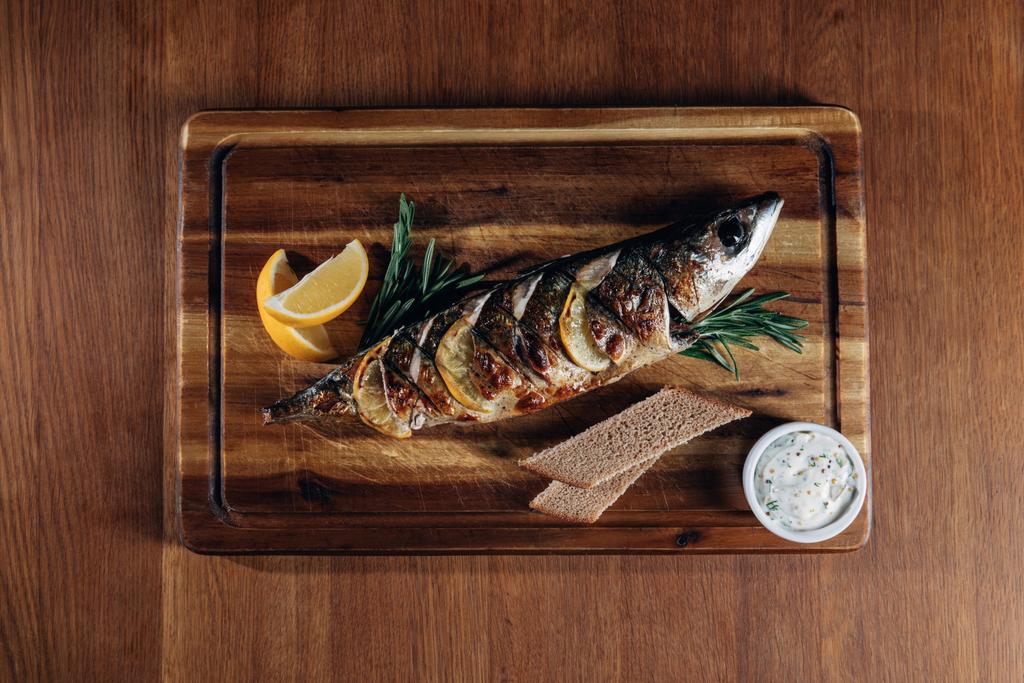 top view of grilled fish with lemon and rye bread on wooden board - Photo, Image