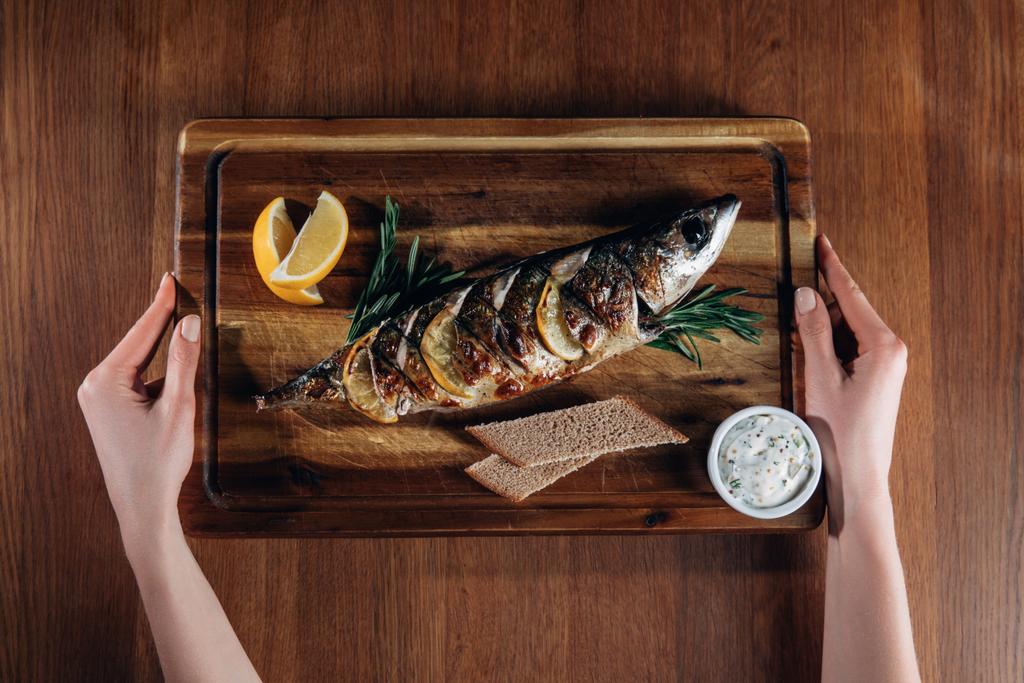 cropped shot of woman holding grilled fish with lemon on wooden board - Photo, Image