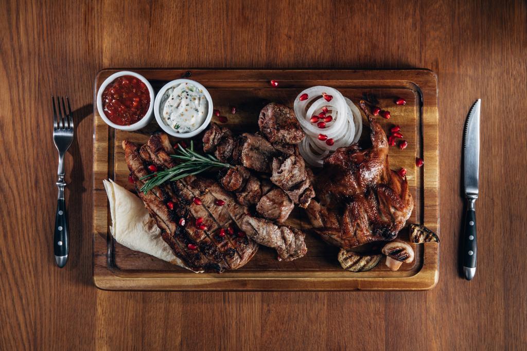 ανάμεικτα ψητά κρέατα σερβίρονται σε ξύλινη σανίδα με σάλτσες - Φωτογραφία, εικόνα