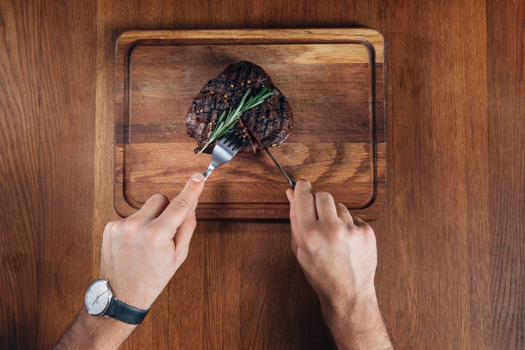 tiro cortado de homem cortando bife grelhado na placa de madeira
 - Foto, Imagem
