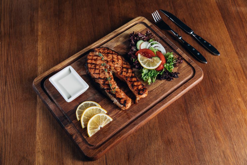 grillezett lazac steak tálalva fából készült táblán citrom és saláta - Fotó, kép