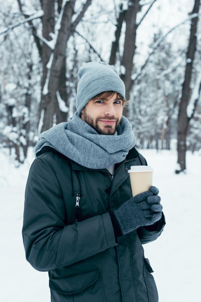 portrét pohledný mladý muž s kávou v ruce v zasněženém parku - Fotografie, Obrázek
