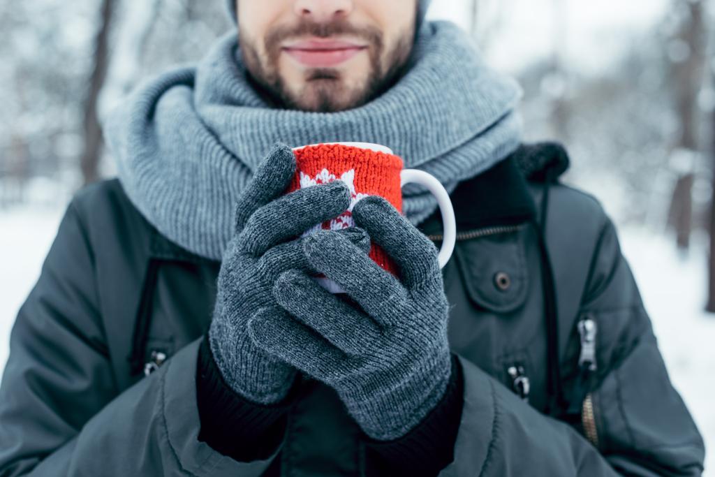 vista parziale dell'uomo che tiene in mano una tazza di caffè caldo nelle mani nella giornata invernale nel parco
 - Foto, immagini