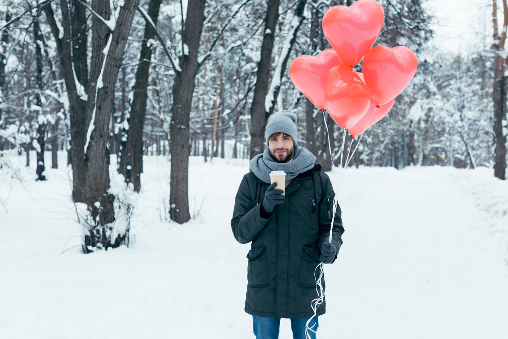портрет молодого чоловіка з кавою, щоб піти і повітряні кулі у формі серця в зимовому парку
 - Фото, зображення