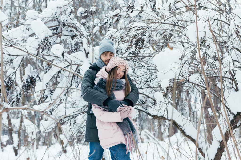 Молодой человек обнимает девушку в зимнем лесу
 - Фото, изображение