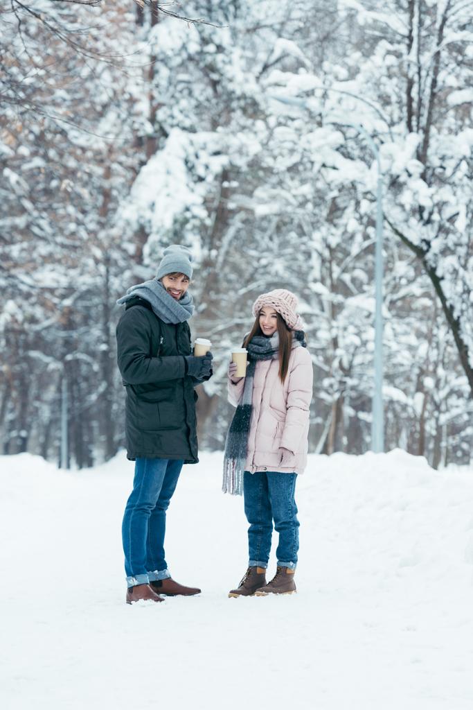 χαρούμενο ζευγάρι με τον καφέ να πάμε στέκεται στο χιονισμένο πάρκο - Φωτογραφία, εικόνα