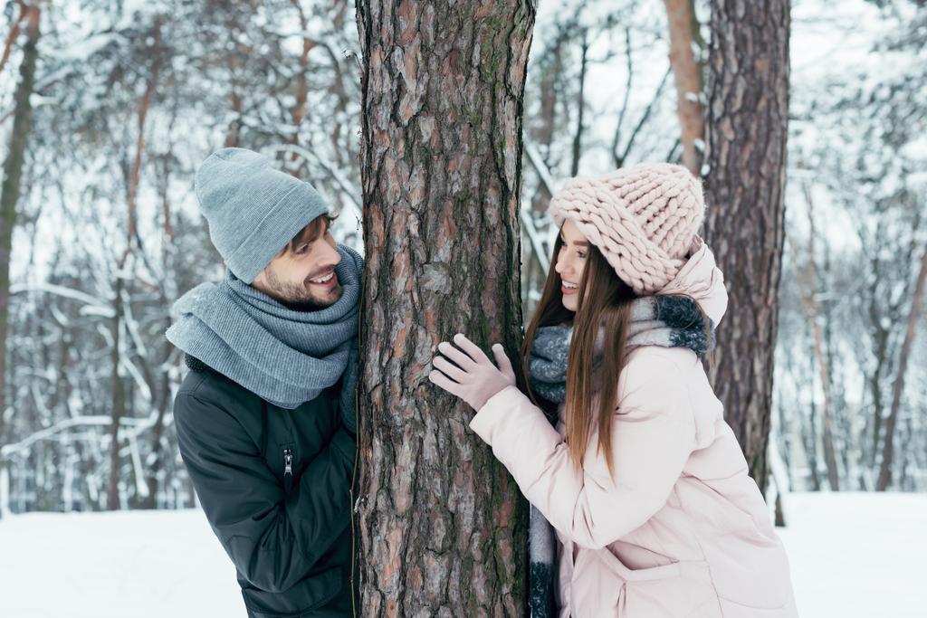 веселая молодая пара, стоящая у дерева в зимнем парке
 - Фото, изображение